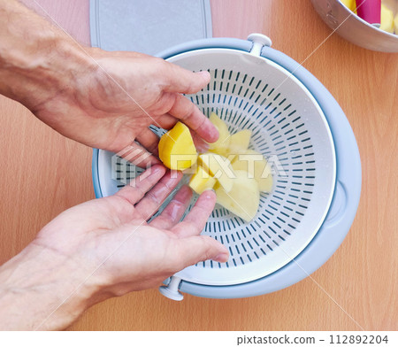 Close up of man holding and peeling potato. Hands cutting potatoes at kitchen to prepare a recipe. Close up of man holding and peeling potato. Hands cutting potatoes at kitchen to prepare a recipe. 112892204