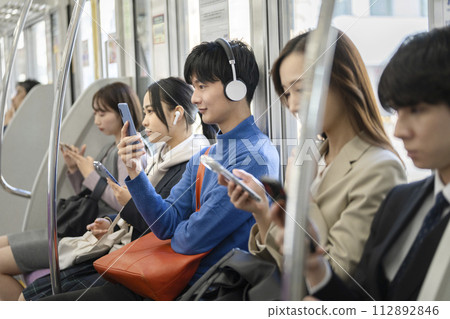 Passenger on the train: Young man wearing headphones looking at smartphone screen 112892846