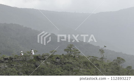 Hikers with White Raincoats Walking on Misty Mountain Ridge 112893227