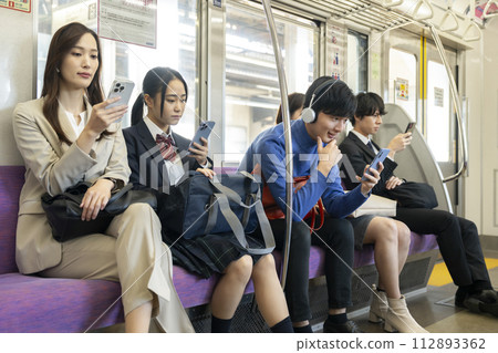 Train passengers looking at smartphone screens Train passengers looking at smartphone screens 112893362