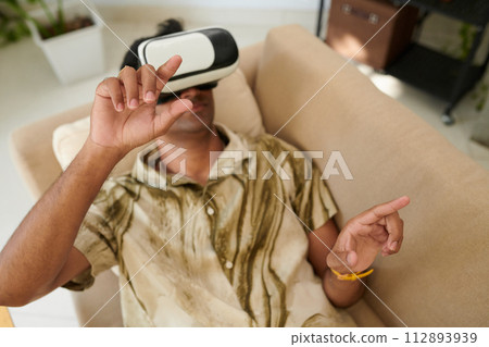 Man in virtual reality headset lying on couch and playing videogame or working Man in virtual reality headset lying on couch and playing videogame or working 112893939