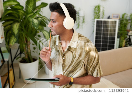 Contemplative man listening to podcast about solar energy and taking notes 112893941