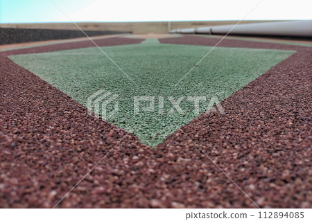 A green arrow pointing downwards to a wall of a house made of red green stone chips looking at an uneven surface, as an element of decorating the facade of buildings 112894085