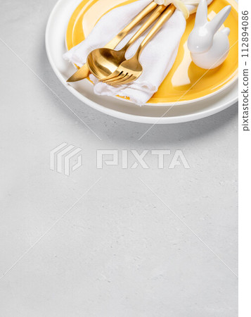Card for Easter menu. Yellow and white plates, white napkin, gold cutlery, ceramic bunny. Copy space 112894086