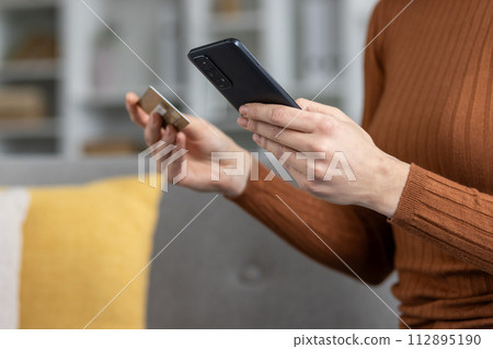 Woman using smartphone and credit card for online shopping with focus on hands and devices. 112895190