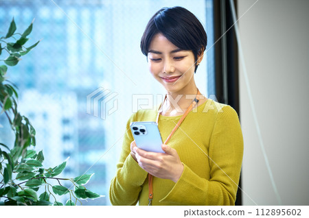 穿著西裝的中層女商人在辦公室操作智能手機 穿著西裝的中層女商人在辦公室操作智能手機 112895602