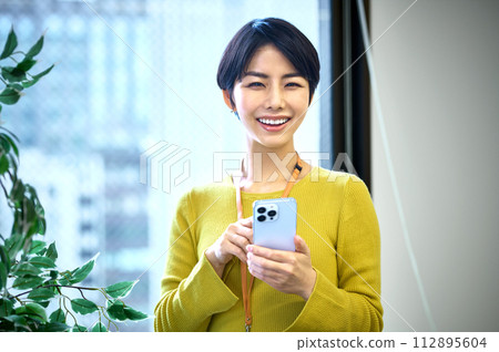 穿著西裝的中層女商人在辦公室操作智能手機 穿著西裝的中層女商人在辦公室操作智能手機 112895604