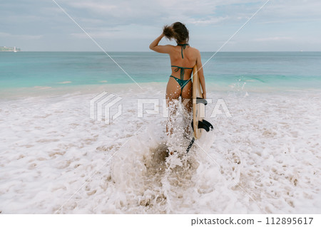 Surfgirl with surfboard goes to surfing. Surfer woman in sexy bikini on ocean beach 112895617