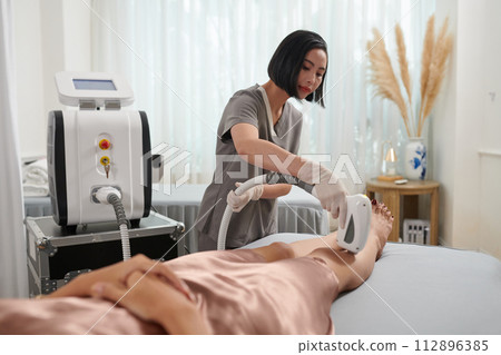 Beautician epilating legs of female client Beautician epilating legs of female client 112896385