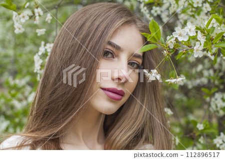 Attractive young woman with natural makeup and healthy long brown hair in blossom park outdoors 112896517