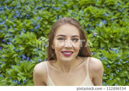 Smiling young woman with natural makeup and healthy long brown hair in blossom park outdoors. 112896534