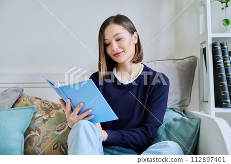 Young woman reading book, relaxed sitting on couch at home 112897401