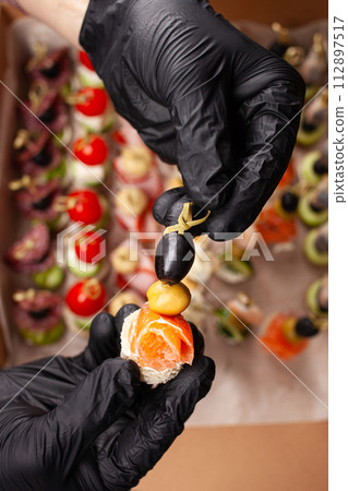 Canape, hands in black gloves hold a beautiful canape on a cap. Catering, snacking, food. Studio photo. Canape, hands in black gloves hold a beautiful canape on a cap. Catering, snacking, food. Studio photo. 112897517