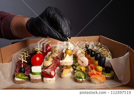Canape, hands in black gloves hold a beautiful canape on a cap. Catering, snacking, food. Studio photo. Canape, hands in black gloves hold a beautiful canape on a cap. Catering, snacking, food. Studio photo. 112897519