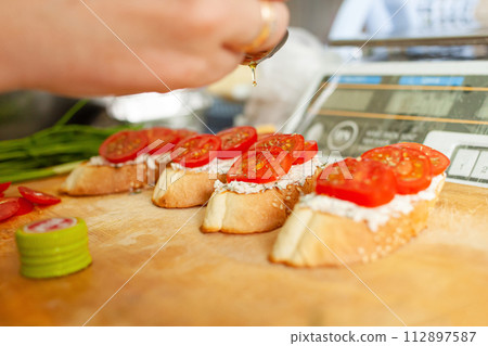 Bruschetta with tomatoes, Philadelphia cheese, sausage, dill and olive oil. The man pours bruschetta with oil. 112897587