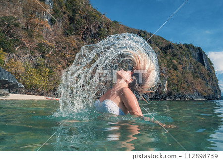 Woman Flipping Her Hair in Clear Waters Near a Rocky Cliff on a Sunny Day Woman Flipping Her Hair in Clear Waters Near a Rocky Cliff on a Sunny Day 112898739