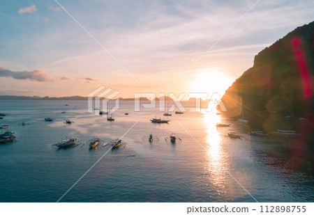 Aerial view of cliffs in the sea, yachts are sailing nearby, mountains covered with tropical forest. El Nido, Palawan, Philippines. Aerial view of cliffs in the sea, yachts are sailing nearby, mountains covered with tropical forest. El Nido, Palawan, Philippines. 112898755