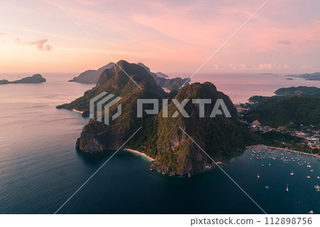 Aerial view of cliffs in the sea, yachts are sailing nearby, mountains covered with tropical forest. El Nido, Palawan, Philippines. Aerial view of cliffs in the sea, yachts are sailing nearby, mountains covered with tropical forest. El Nido, Palawan, Philippines. 112898756