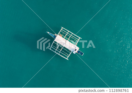 Aerial drone view of boat anchored in the bay with clear and turquoise water on the sunset. Boat in the tropical lagoon. Tropical landscape. El Nido, Palawan island, Philippines. Aerial drone view of boat anchored in the bay with clear and turquoise water on the sunset. Boat in the tropical lagoon. Tropical landscape. El Nido, Palawan island, Philippines. 112898761