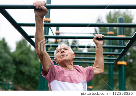 Senior man climbing on horizontal ladder in outdoor workout station Senior man climbing on horizontal ladder in outdoor workout station 112898820