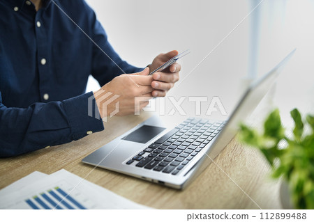 一名中年男子一邊看電腦一邊操作智慧型手機的手 112899488