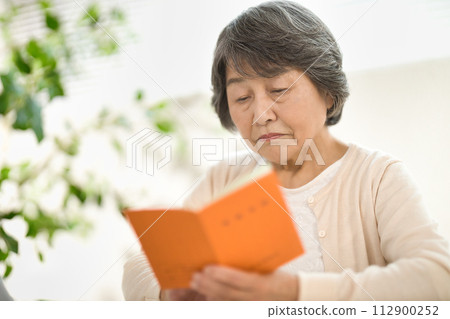 A senior woman using a computer while looking at her pension notebook, ending her life A senior woman using a computer while looking at her pension notebook, ending her life 112900252