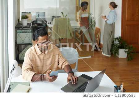 Serious developer testing mobile app performance when his colleagues chatting in background Serious developer testing mobile app performance when his colleagues chatting in background 112900585