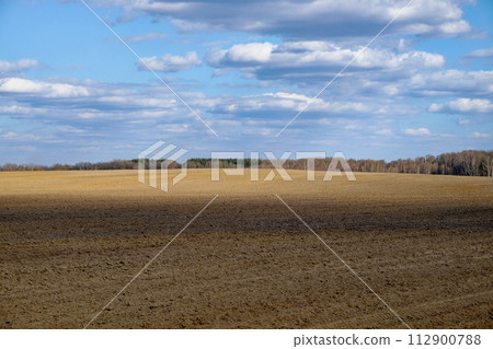 The image shows an expansive ploughed field under a cloudy sky. 112900788