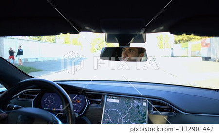 Eyes of male driver reflecting of rearview mirror during riding electrical auto. Confident man driving a modern car at city. Young guy looking concentrated to urban road during operating vehicle 112901442