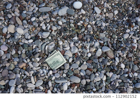 Hundred dollars half covered with round rocks lie on beach close up. Dollar bills partially buried in sea shore stones. Concept finance money holiday relax vacation and money losing in travel Hundred dollars half covered with round rocks lie on beach close up. Dollar bills partially buried in sea shore stones. Concept finance money holiday relax vacation and money losing in travel 112902152