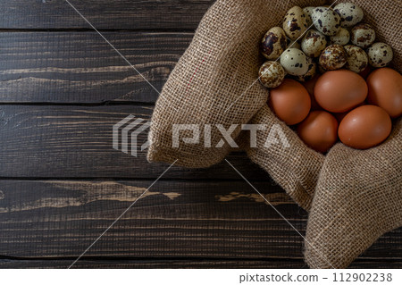 Fresh chicken and quail eggs in a basket on a sack, wooden table.Selective focus 112902238