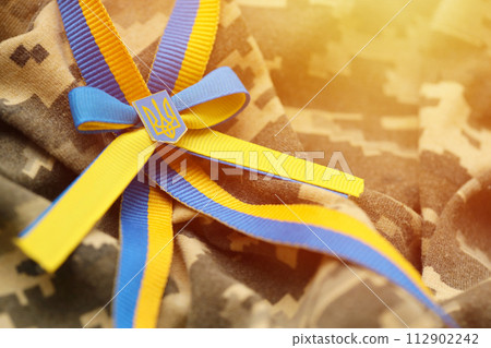 Pixeled digital military camouflage fabric with ukrainian flag and coat of arms on stripes ribbon in blue and yellow colors. Attributes of ukrainian soldier uniform Pixeled digital military camouflage fabric with ukrainian flag and coat of arms on stripes ribbon in blue and yellow colors. Attributes of ukrainian soldier uniform 112902242