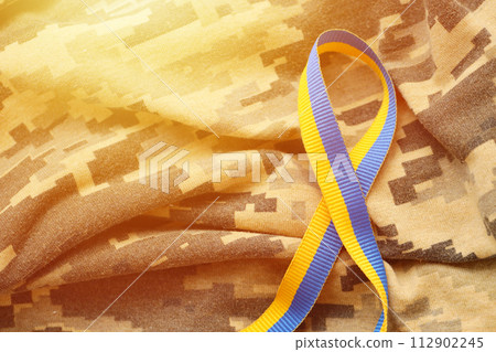 Pixeled digital military camouflage fabric with ribbon in blue and yellow colors. Attributes of ukrainian patriotic soldier uniform Pixeled digital military camouflage fabric with ribbon in blue and yellow colors. Attributes of ukrainian patriotic soldier uniform 112902245