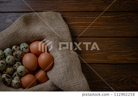 Fresh chicken and quail eggs in a basket on a sack, wooden table.Selective focus 112902258