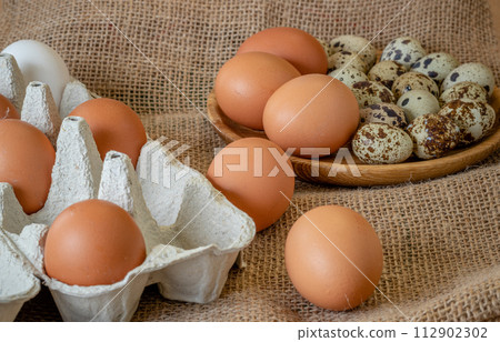 Fresh chicken and quail eggs in tray, plate on wooden board, selective focus 112902302