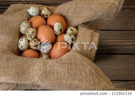 Fresh chicken and quail eggs in a basket on a sack, wooden table.Selective focus Fresh chicken and quail eggs in a basket on a sack, wooden table.Selective focus 112902316