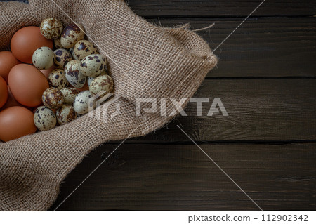 Fresh chicken and quail eggs in a basket on a sack, wooden table.Selective focus Fresh chicken and quail eggs in a basket on a sack, wooden table.Selective focus 112902342