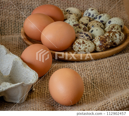 Fresh chicken and quail eggs in tray, plate on wooden board, selective focus 112902457