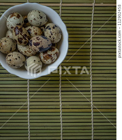 Fresh quail eggs in a white deep plate on a wooden table, selective focus Fresh quail eggs in a white deep plate on a wooden table, selective focus 112902458