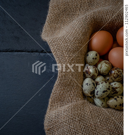 Fresh chicken and quail eggs in a basket on a sack, wooden table.Selective focus 112902465