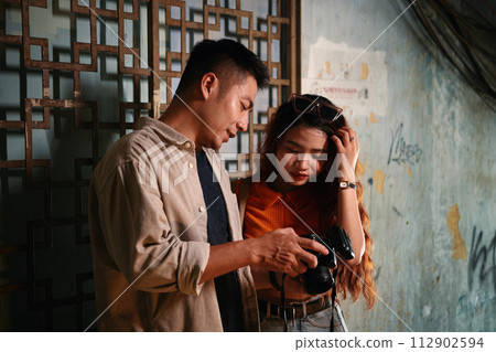 Vietnamese young man showing photos on screen of digital camera to girlfriend after shoot in old building Vietnamese young man showing photos on screen of digital camera to girlfriend after shoot in old building 112902594