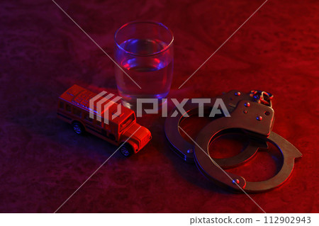 Glass with vodka alcohol drink, handcuffs and yellow toy school bus. School criminality and alcoholism concept 112902943