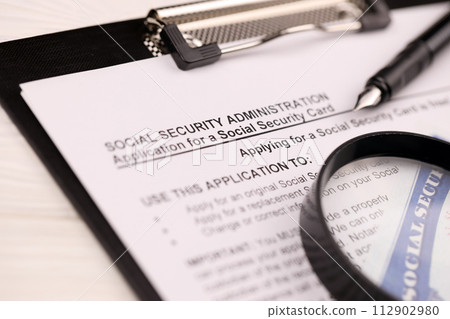 United States social security number cards lies on Application from social security administration on A4 tablet lies on office table with pen and magnifying glass close up United States social security number cards lies on Application from social security administration on A4 tablet lies on office table with pen and magnifying glass close up 112902980