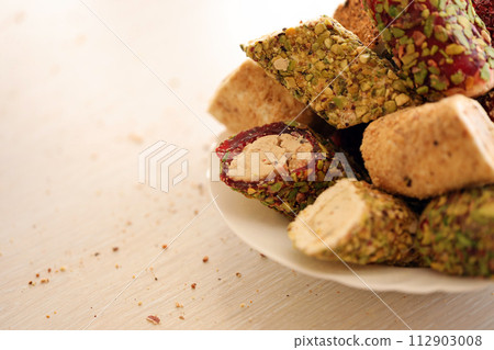 Many rolls of turkish delight with different flavors and fillings in white plate on table. Cuts of Turk Lokumu sweets 112903008