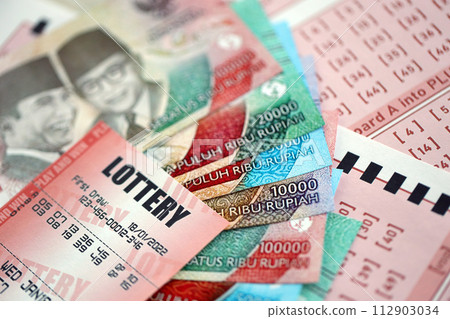 Red lottery ticket lies on pink gambling sheets with indonesian rupiah money bills. Lottery playing concept or gambling addiction in indonesia 112903034