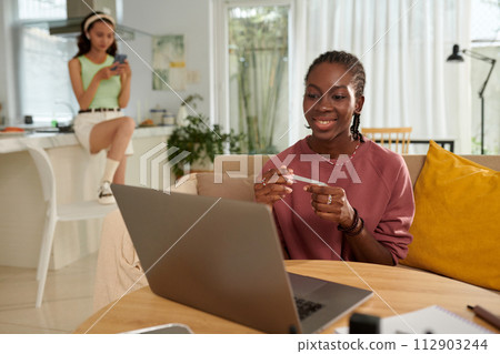Smiling Black girl filing nails when watching show on laptop at home 112903244