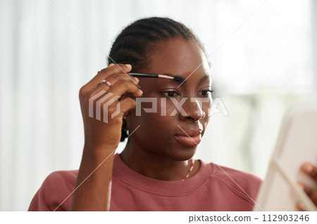 Black teenage girl brushing eyebrows and applying fixing gel Black teenage girl brushing eyebrows and applying fixing gel 112903246