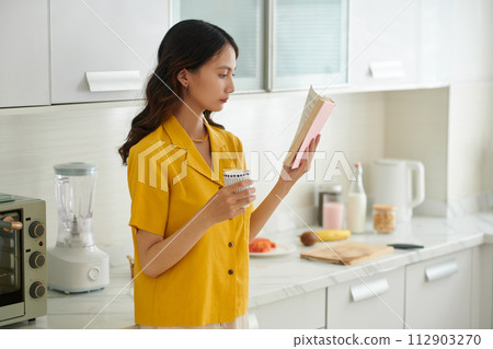 Serious young Vietnamese woman drinking morning coffee and reading book 112903270