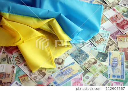 Ukrainian flag on many banknotes of different currency. Background of war funding and military support price in Ukraine Ukrainian flag on many banknotes of different currency. Background of war funding and military support price in Ukraine 112903367