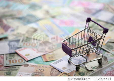 Supermarket trolley on many banknotes of different currency. Background of shopping worldwide close up Supermarket trolley on many banknotes of different currency. Background of shopping worldwide close up 112903371